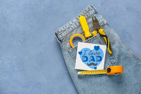 Jeans with tools and postcard for Father's Day on blue grunge background