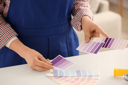 Young woman choosing violet paint palette swatches near table at home, closeupの写真素材