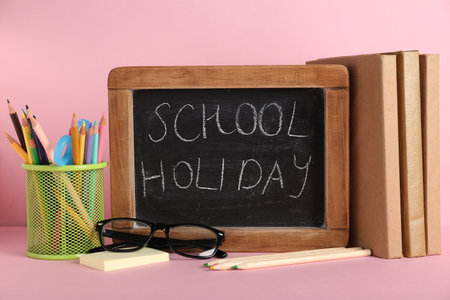 Chalkboard with text SCHOOL HOLIDAY and different stationery supplies on pink backgroundの写真素材