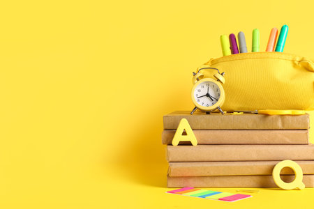 Different school stationery with alarm clock and books on yellow background