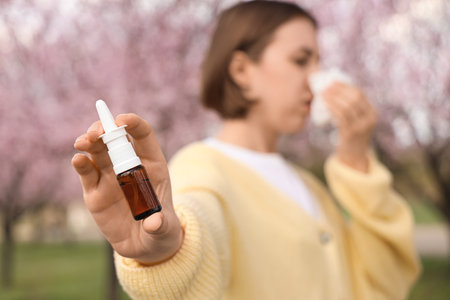 Allergic young woman with tissue and nasal drops sneezing in park, closeupの写真素材