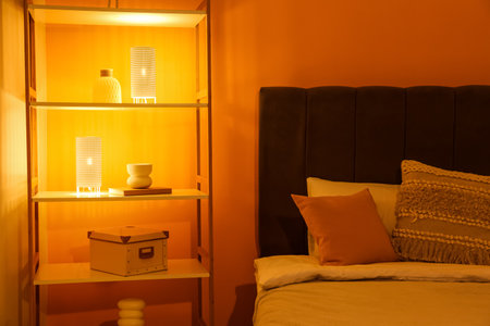 Interior of night bedroom with big bed, shelving unit and glowing lamps near orange wallの写真素材
