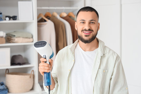 Young man with steamer in bedroomの写真素材