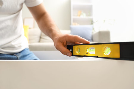 Young man with level assembling shelf unit at home, closeup