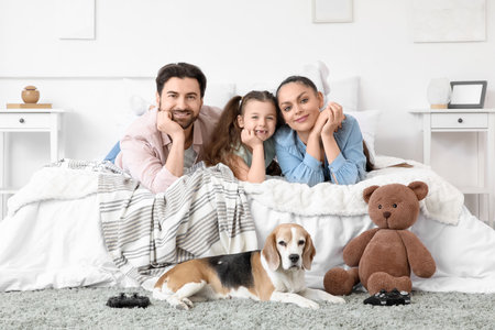Cute little girl with her parents and Beagle dog lying in bedroomの写真素材