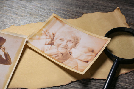 Old photos of relatives with magnifier on wooden background, closeup. Concept of family tree