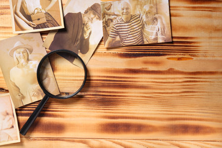Old photos of relatives with magnifier on wooden background with space for text. Concept of family treeの写真素材
