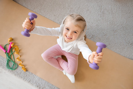 Sporty little girl in headphones training with dumbbells at home, top viewの写真素材