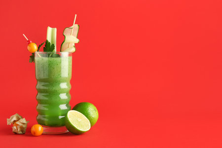 Glass of green cocktail garnished with berries, celery and cucumber slice on red backgroundの写真素材