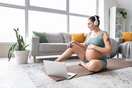 Sporty pregnant woman in headphones massaging her leg with ball on mat at homeの写真素材