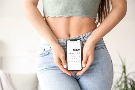 Young woman holding mobile phone with menstrual calendar at home, closeupの写真素材