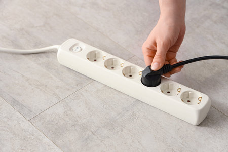 Female hand getting out plug from extension cord on floor, closeup