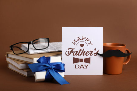 Card with text HAPPY FATHER'S DAY, cup, gift box, books and eyeglasses on color backgroundの写真素材