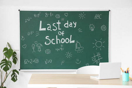 Blackboard with text LAST DAY OF SCHOOL and drawings on light wall in classroomの写真素材