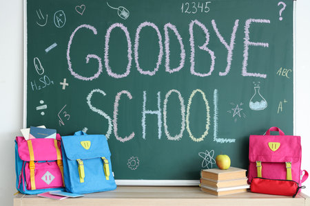 Backpacks with books and text GOODBYE SCHOOL on blackboard in classroomの写真素材