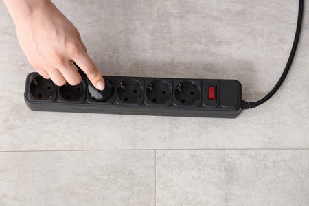 Female hand getting out plug from extension cord on floor, top view