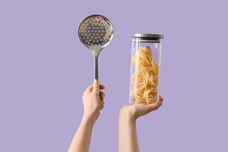 Female hands with ladle and jar of pasta on lilac background