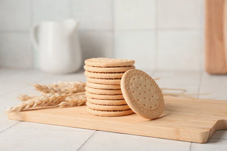 Wooden board with sweet cookies and wheat on white tile backgroundの写真素材