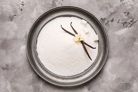 Plate of sweet vanilla sugar on grunge background, top view