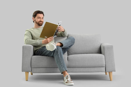 Handsome man reading magazine on sofa against light backgroundの写真素材