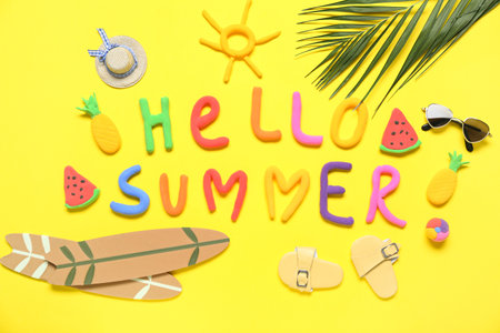 Composition with text HELLO SUMMER, mini beach accessories and palm leaf on yellow backgroundの写真素材