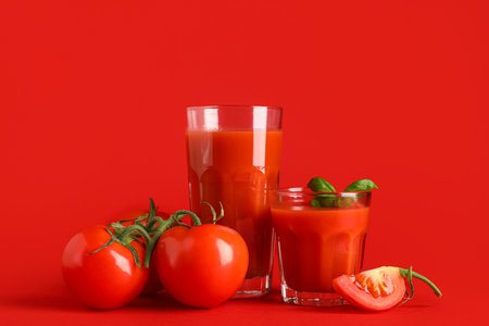 Glasses of fresh tomato juice with basil on red backgroundの写真素材