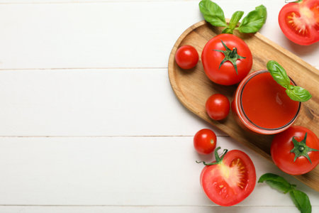 Glass of fresh tomato juice with basil and vegetables on white wooden backgroundの写真素材