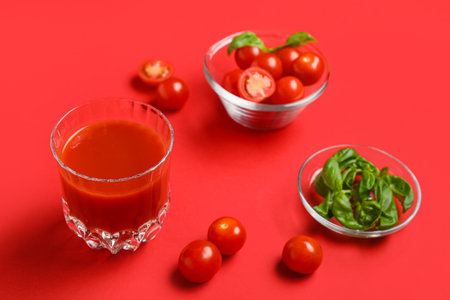 Glass of fresh tomato juice with basil and vegetables on red background, closeupの写真素材