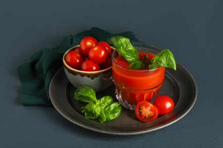 Glass of fresh tomato juice with basil and vegetables on dark backgroundの写真素材