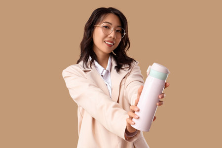 Young Asian businesswoman with thermos on beige backgroundの写真素材