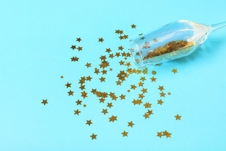 Champagne glass with beautiful golden confetti in shape of star on blue background, closeupの写真素材