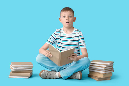 Surprised little boy with books sitting on color backgroundの写真素材