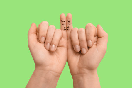 Female hands with drawn faces on her pinkie fingers on green background, closeup. Friendship Day celebrationの写真素材