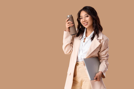 Young Asian businesswoman with thermos and laptop on beige backgroundの写真素材