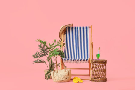 Striped deck chair with glass of cocktail, beach bag and flip flops on pink background
