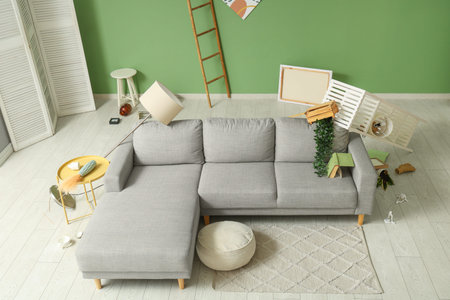 Interior of messy living room with gray sofa, overturned shelving unit and scattered belongings...