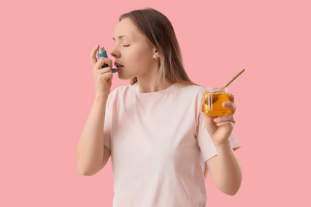 Young woman with honey using asthma inhaler on pink background. Food Allergy Awareness Month