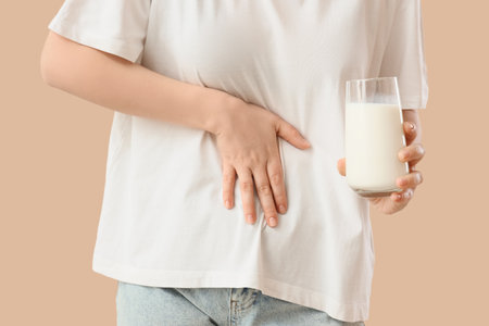 Young woman with bellyache and glass of milk on beige background, closeup. Food Allergy Awareness Monthの写真素材