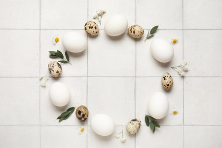 Frame made from Easter eggs, flowers and leaves on white tiled backgroundの写真素材