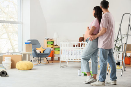 Young pregnant couple hugging during repair in children's room, back viewの写真素材