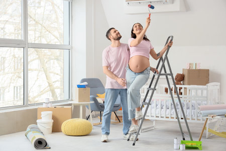 Young pregnant couple with paint roller doing repairs in children's roomの写真素材