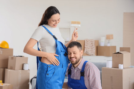 Young man listening to his pregnant wife's belly during repair in roomの写真素材