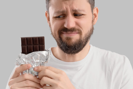 Young man with chocolate bar on light background, closeup. Food Allergy Awareness Month