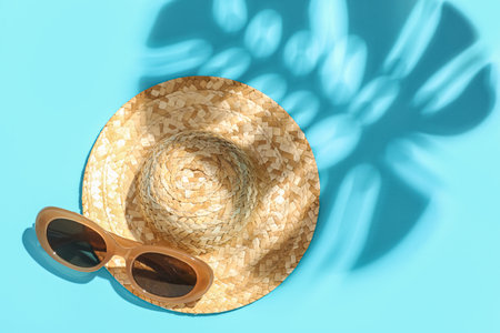 Stylish sunglasses, straw hat and palm leaf shadow on color backgroundの写真素材