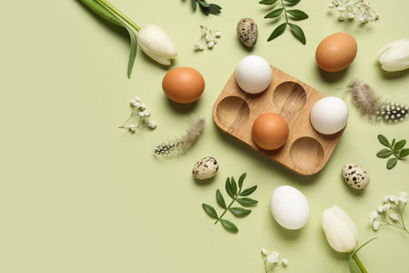 Composition with egg holder, Easter eggs, green leaves and feathers on green backgroundの写真素材