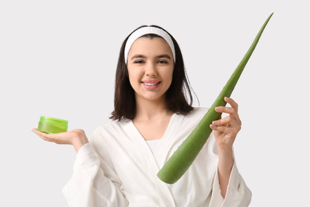 Happy young woman in bathrobe and headband with aloe vera leaf and jar of gel on white backgroundの写真素材