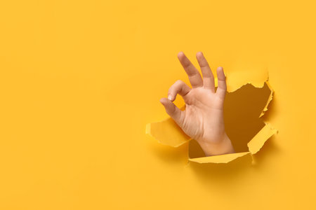 Female hand showing OK visible through hole in yellow paperの写真素材