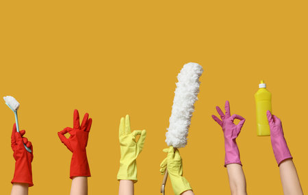 Female hands in rubber gloves with cleaning supplies showing OK on yellow background