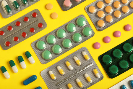 Different pills in blister packs on yellow background