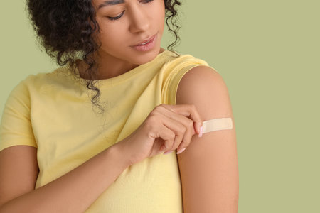 Young African-American woman with medical patch after vaccination on green backgroundの写真素材